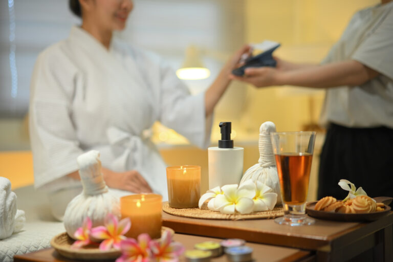 Spa still life with herbal compress and welcome drink with woman paying with card in background